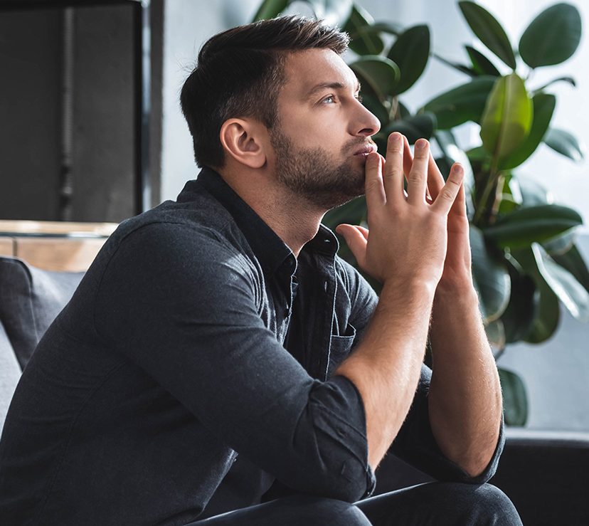 Photo of a man in dark clothes, sitting and thinking on the couch