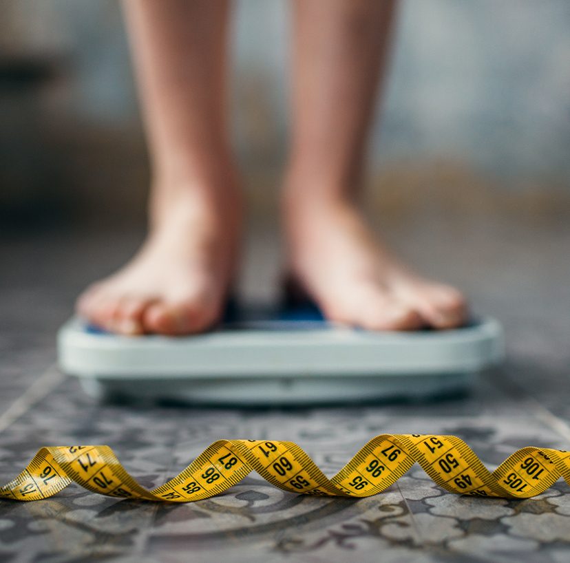 Photo of someone standing on a scale, with measuring tape on the ground