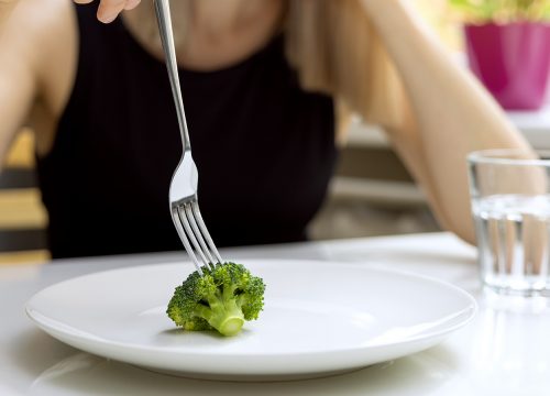 Photo of a woman using a fork to pick up a stem of broccoli