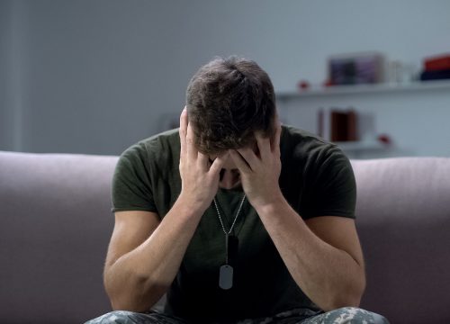 Photo of a male army vet sitting on a couch at home, dealing with PTSD