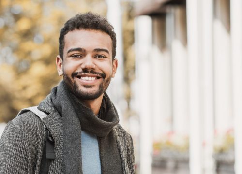 Photo of a smiling man standing outside wearing a coat and scarf