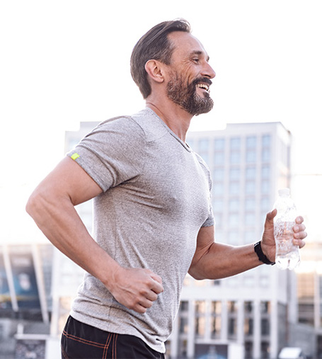 Photo of a man jogging through a city holding a bottle of water