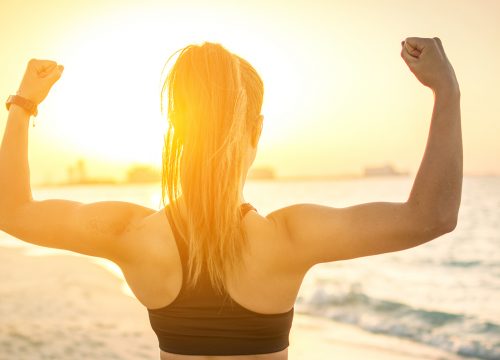 Woman flexing on the beach during a sunrise.