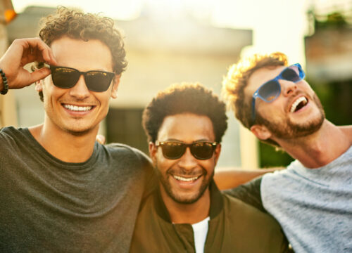 Photo of three male friends smiling and laughing outside in the sun