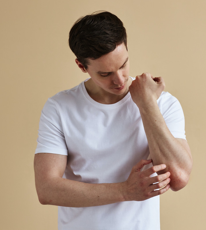 Photo of a man with an autoimmune disease scratching his arm